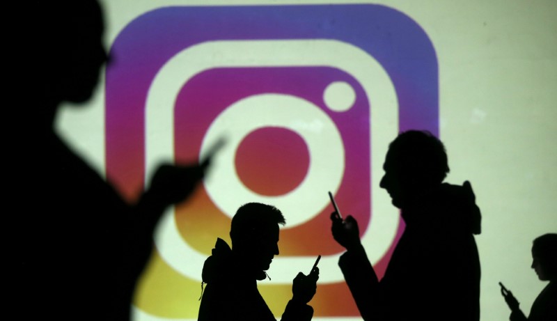 Silhouettes of mobile users are seen next to a screen projection of Instagram logo in this picture illustration