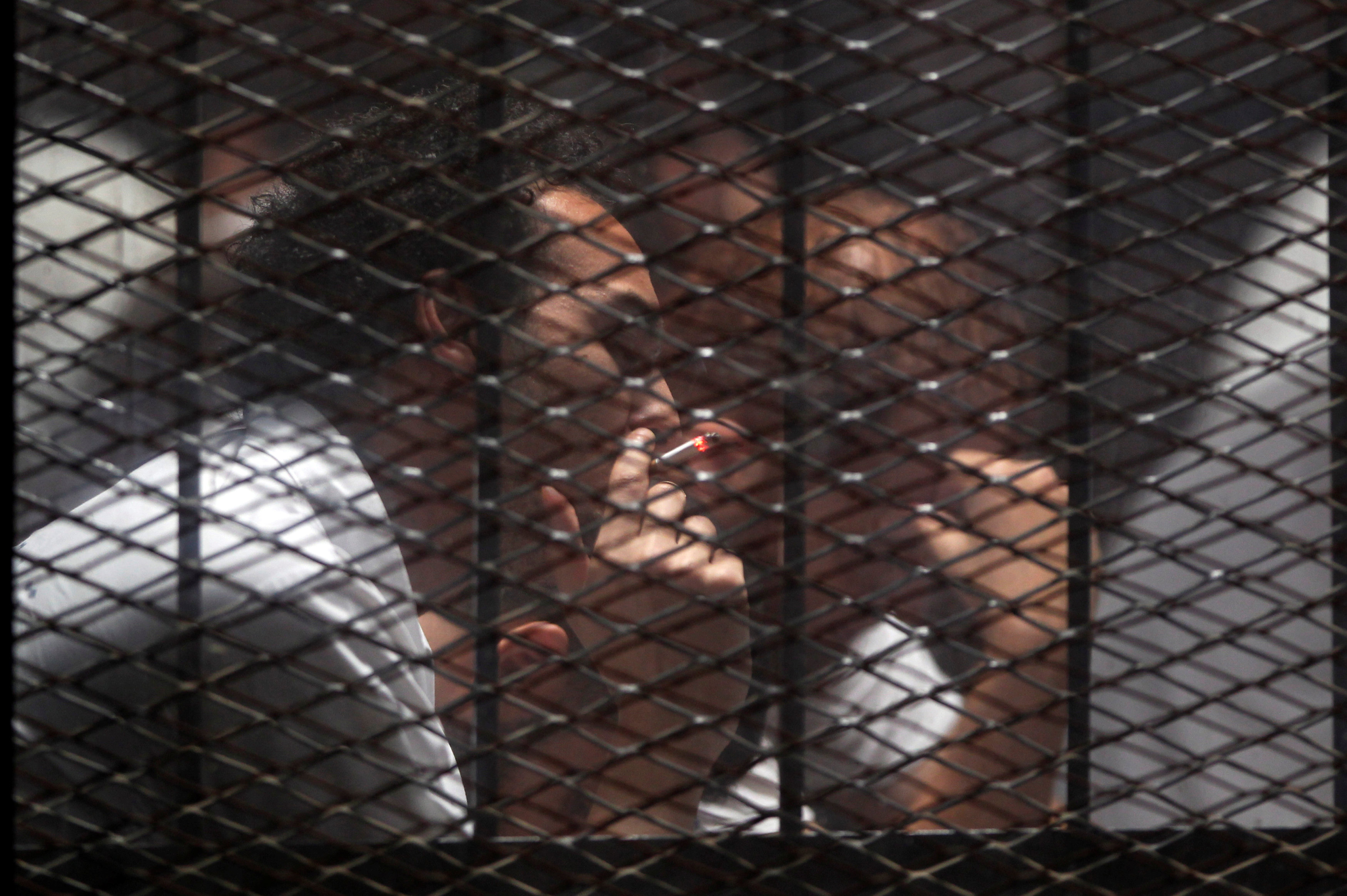 Egyptian photojournalist Mahmoud Abu Zeid, also known as Shawkan, smokes cigarette behind a fence during his trial in Cairo