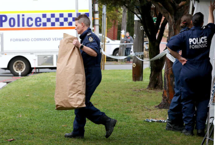 A police officer carries a bag from a property where five people were found dead in a suburb of Perth