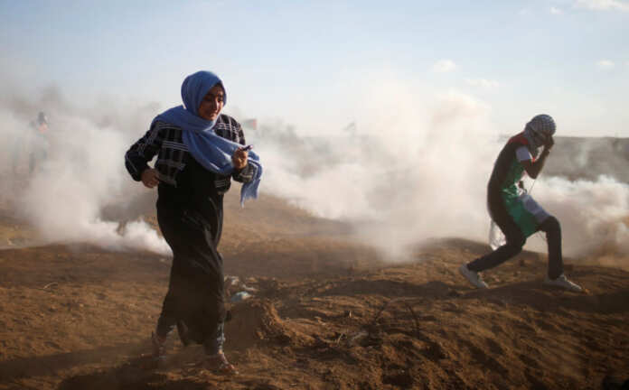 Palestinians run from tear gas fired by Israeli troops during a protest at the Israel-Gaza border fence, east of Gaza City