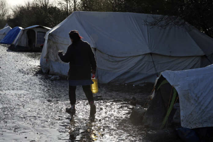 A migrant walks past shelters in a muddy field called the Grande-Synthe jungle near Dunkerque
