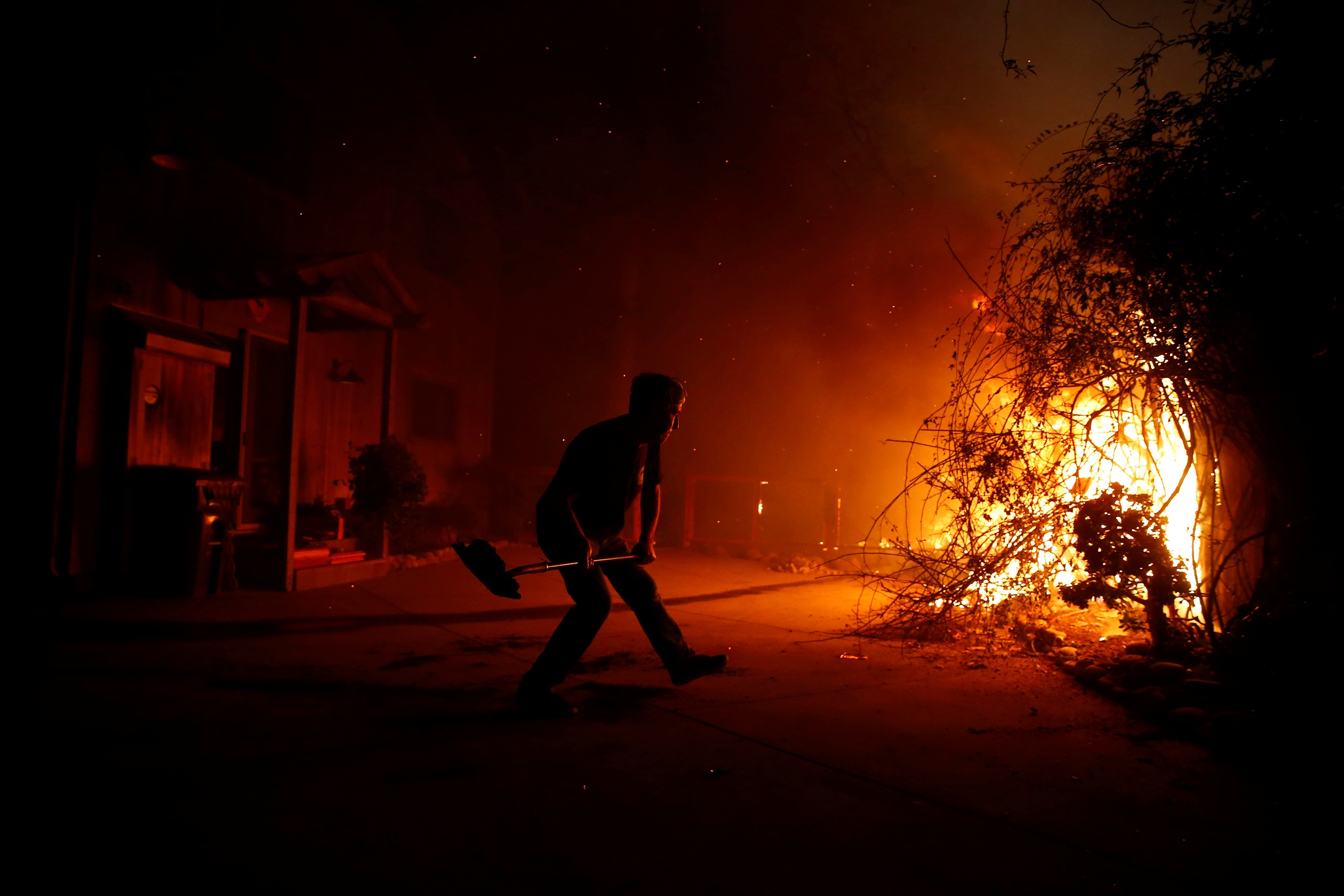A man throws dirt at the fire after losing water pressure while fighting to save his home as the Woolsey Fire burns in Malibu