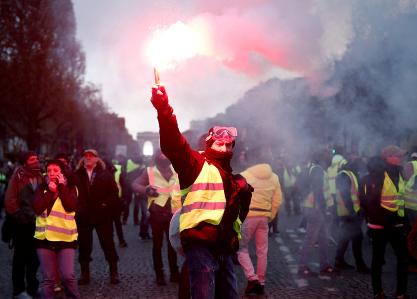 A protester wearing yellow vest, a symbol of a French drivers' protest against higher fuel prices, burns flare on the the Champs-Elysee in Paris