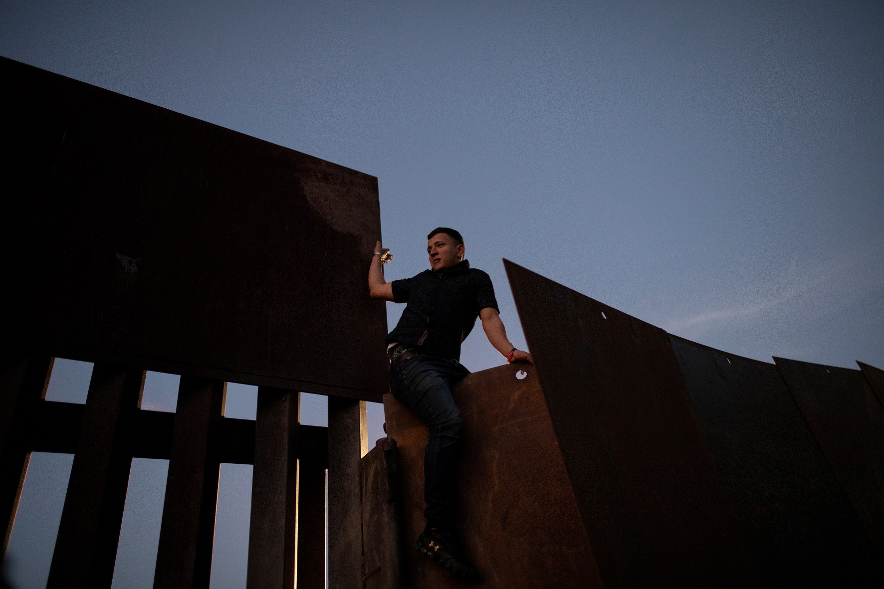 A migrant, part of a caravan of thousands from Central America trying to reach the United States, climbs a border fence to cross illegally from Mexico to the U.S, in Tijuana