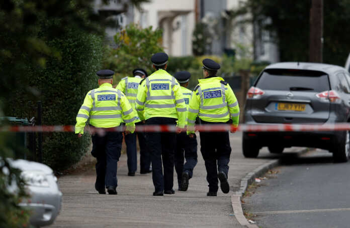 Police officers walk behind cordon tape set up around a property being searched after a man was arrested in connection with an explosion on a London Underground train, in Sunbury-on-Thames