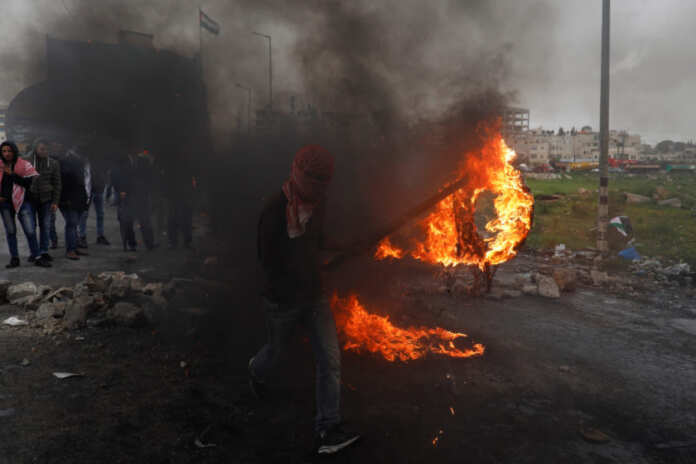 Palestinian demonstrator moves a burning tire during clashes with Israeli forces at a protest marking Land Day, near the Jewish settlement of Beit El, in the Israeli-occupied West Bank