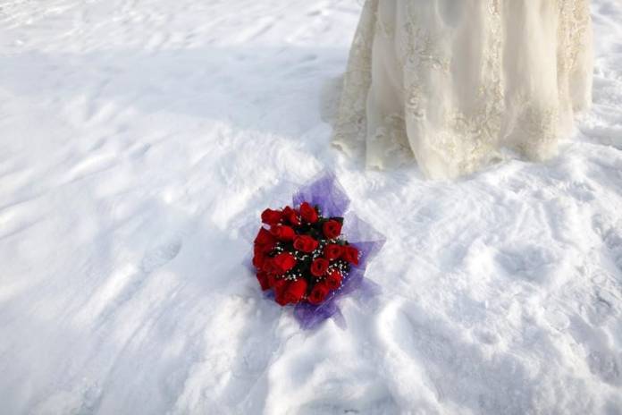 A bouquet is seen in the snow as a bride poses for a photograph after a group wedding ceremony during the 26th Harbin International Ice and Snow Festival in Harbin