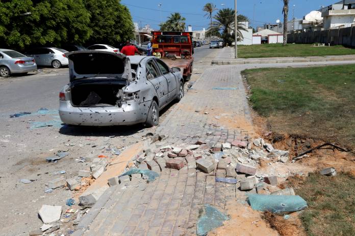 Workers remove a damaged civilian vehicle, after a missile hit the terminal's park of Mitiga airport in Tripoli