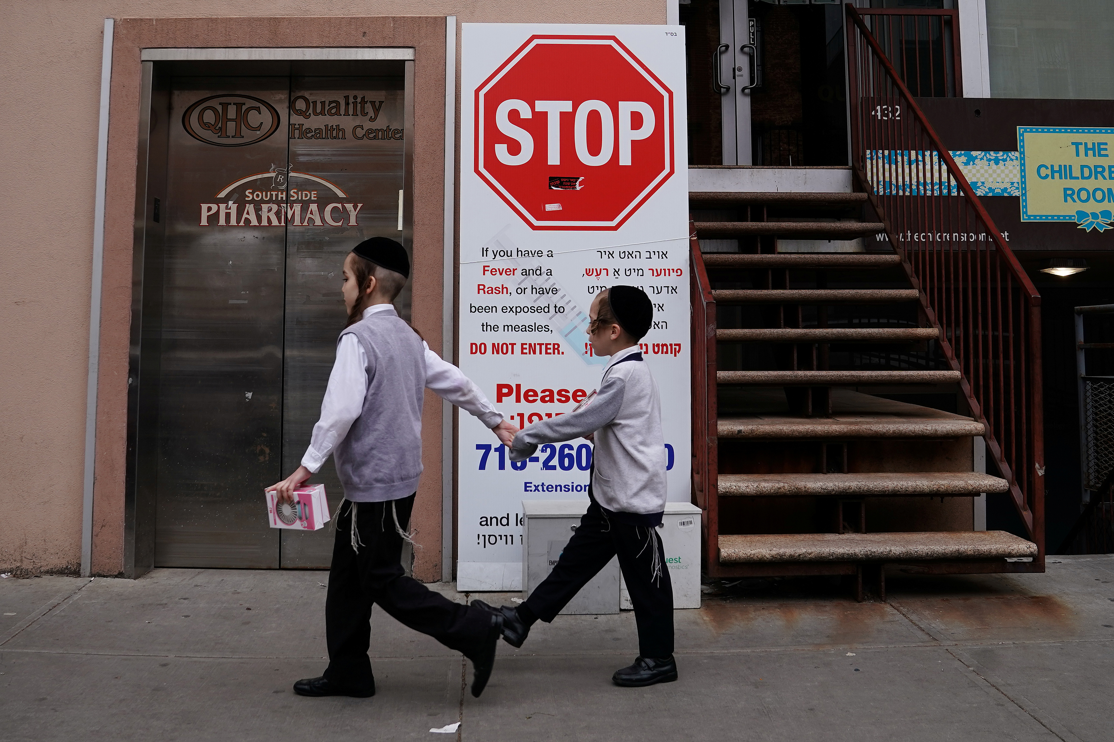 Children walk past a sign advising about a measles outbreak in the Brooklyn Borough of New York