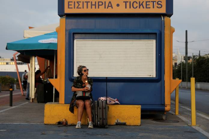 A passenger sits next to a closed ticket booth during a 24-hour general strike at the port of Piraeus