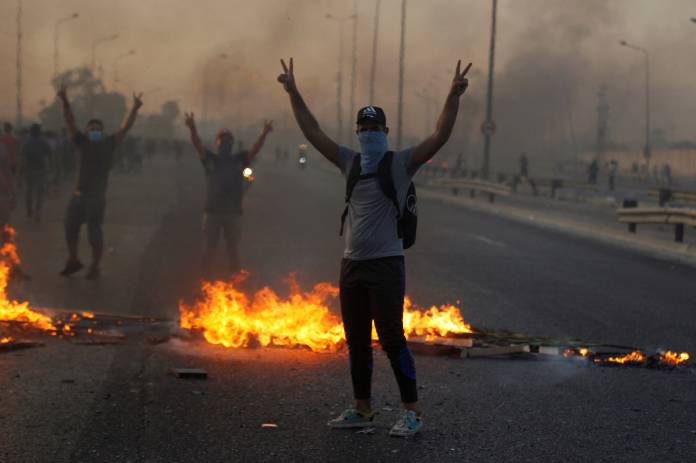 Demonstrators gesture near burning objects at a protest during a curfew, two days after the nationwide anti-government protests turned violent, in Baghdad