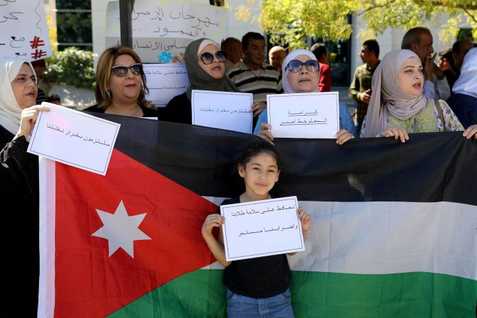 FILE PHOTO - A girl holds placard in front of a Jordanian national flag as public schools' teachers take part in a protest in Amman