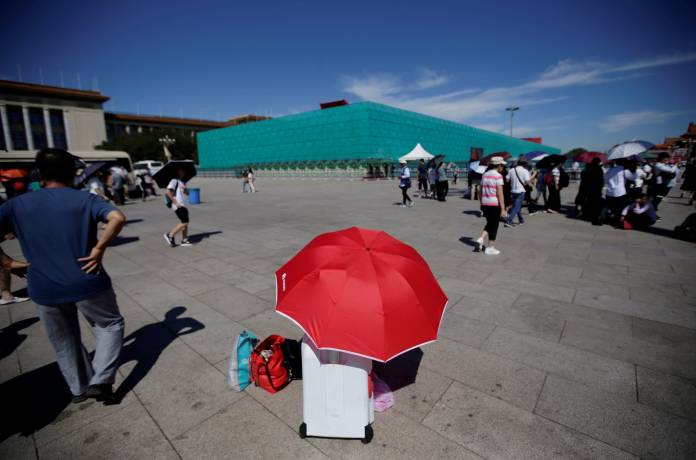FILE PHOTO: A tourist rests under an umbrella next to the installations set up on Tiananmen Square for the 70th anniversary of the founding of People's Republic of China in Beijing