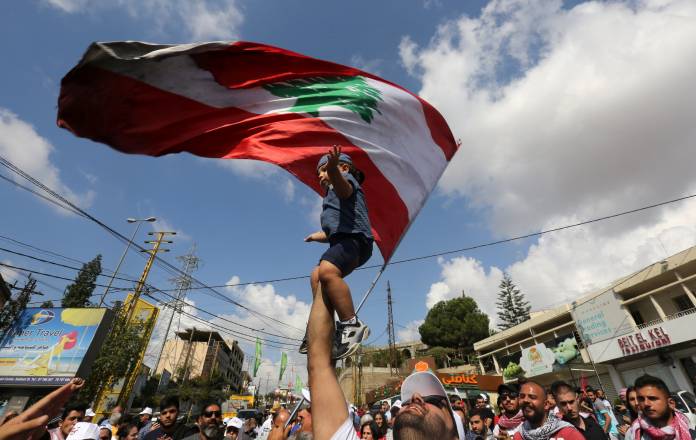 A man lifts a child as demonstrators chant and carry national flag during an anti-government protest in the southern city of Nabatiyeh