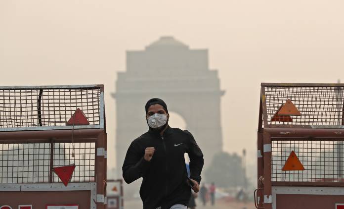 A man wearing a mask runs past the India Gate on a smoggy morning in New Delhi