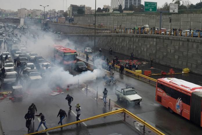 Riot police tries to disperse people as they protest on a highway against increased gas price in Tehran