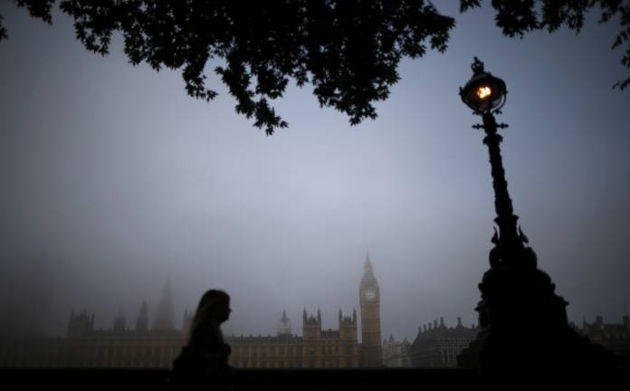 A woman walks along the south bank of the Thames opposite the Houses of Parliament on a foggy morning in London