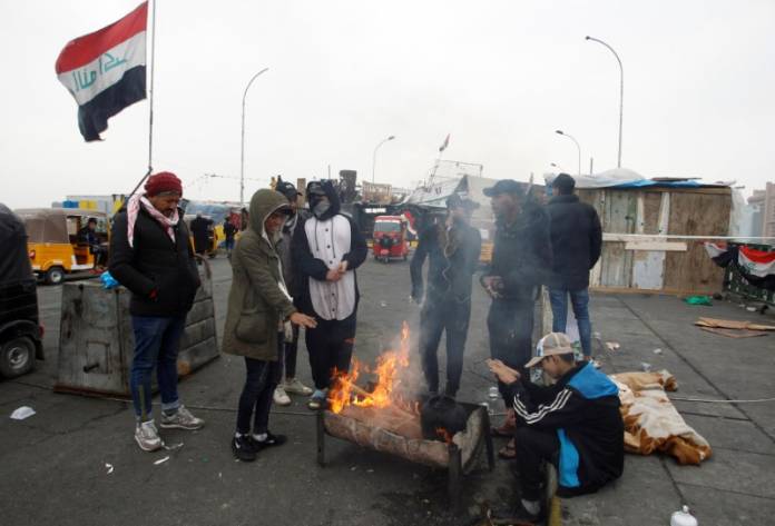 Iraqi demonstrators warm themselves during ongoing anti-government protests, at the Sinak bridge in Baghdad