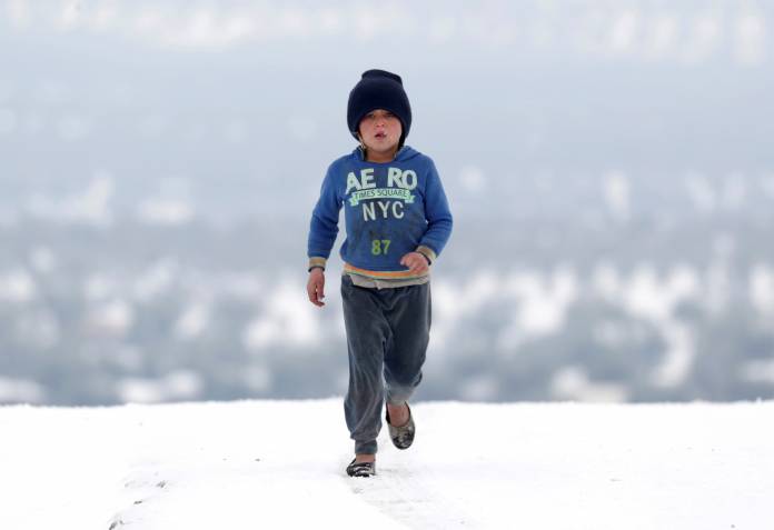 An internally displaced girl walks on snow at a makeshift camp in Azaz