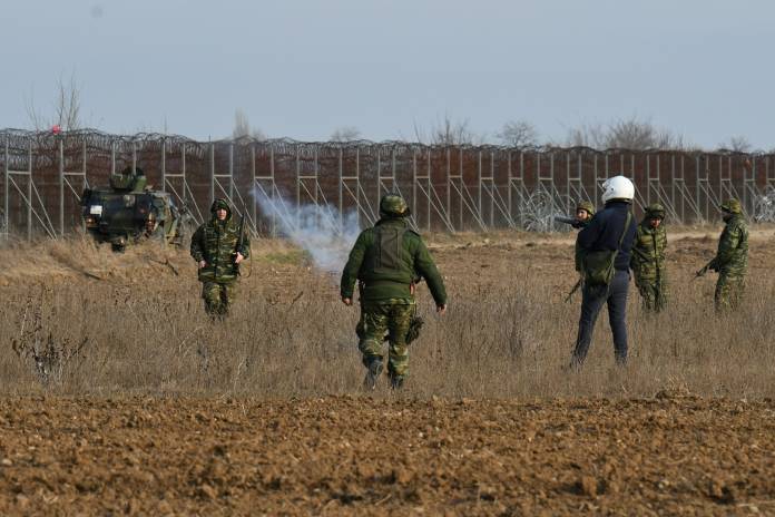 A police officer fires a tear gas canister with his launcher as Greek soldiers stand by, during clashes with migrants who want to cross into Greece from Turkey's Pazarkule border crossing, in Kastanies