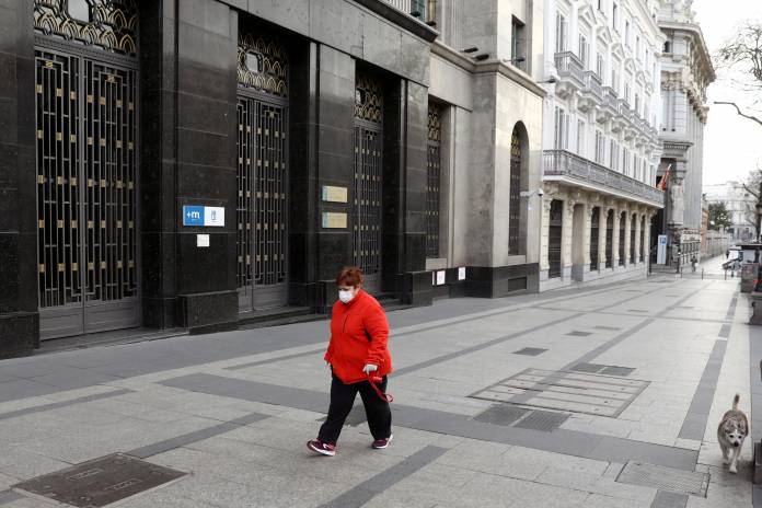 A woman, wearing a protective mask, walks with her dog in the empty Alacal street during partial lockdown, as part of a 15-day state of emergency to combat the coronavirus outbreak in Madrid