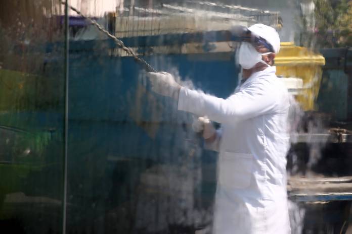 A member of a the medical team wearing a protective face mask is reflected as he sprays disinfectant liquid to sanitise a bus station, following the coronavirus outbreak, in Tehran