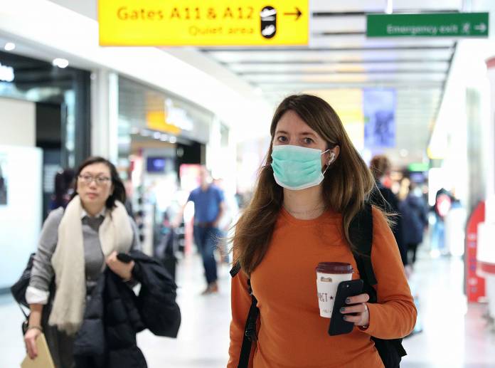 A woman wears a surgical mask as she walks through Terminal 5 at Heathrow Airport in London
