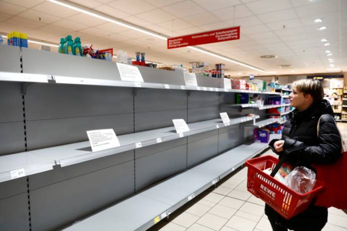 FILE PHOTO: A woman looks at an empty shelf with a sign announcing the rationing of toilet paper at a Rewe grocery store in Potsdam FILE PHOTO: A woman looks at an empty shelf with a sign announcing the rationing of toilet paper at a Rewe grocery store in Potsdam