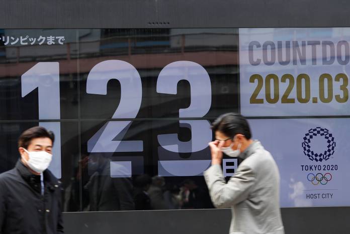 Passersby, wearing face masks due to the outbreak of the coronavirus disease (COVID-19), walk past a screen counting down the days to the Tokyo 2020 Olympic Games in Tokyo Passersby, wearing face masks due to the outbreak of the coronavirus disease (COVID-19), walk past a screen counting down the days to the Tokyo 2020 Olympic Games in Tokyo