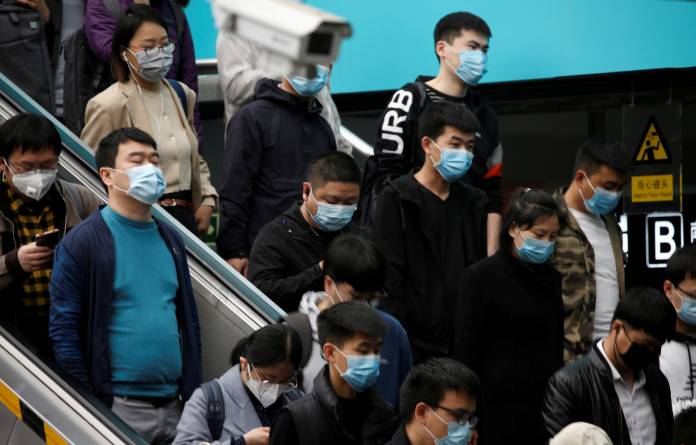 People wearing face masks stand on an escalator inside a subway station during morning rush hour in Beijing