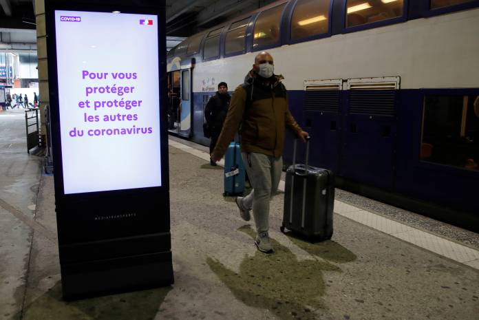 A man wearing a protective face mask walks past an information board about the coronavirus disease at Montparnasse train station in Paris
