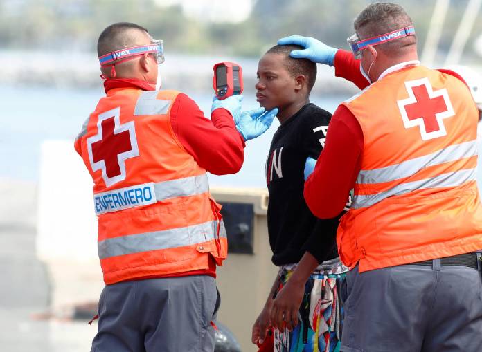 Red Cross members take the temperature of a migrant before disembarking from a Spanish coast guard vessel in the port of Arguineguin on the island of Gran Canaria