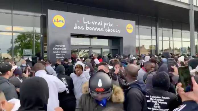 People who gathered outside a Lidl store react after pepper spray was used as the store is due to sell the PlayStation 4 for 95 Euros, in Orgeval