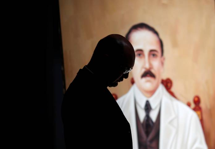 A priest stand in front of a painting depicting Jose Gregorio Hernandez during a mass in Caracas